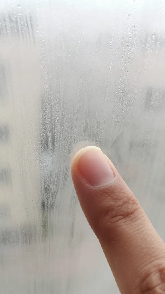 closeup of fingertip wiping condensation trail on glass
